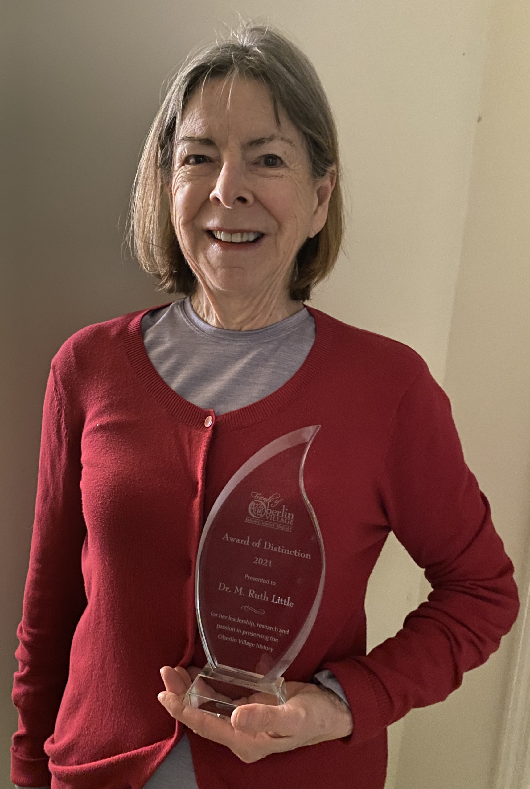 Ruth Little wearing a red sweater holding award