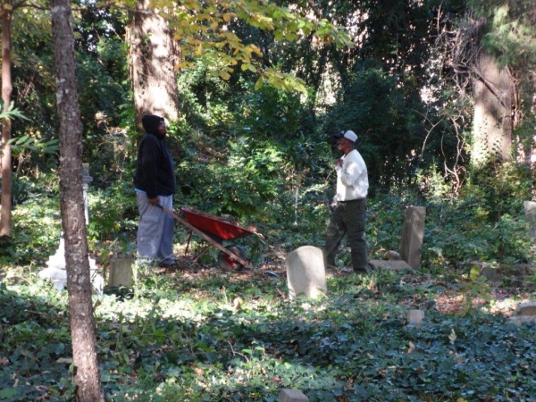 Two volunteers working together with a wheelbarrow to clean up Oberlin Cemetery.