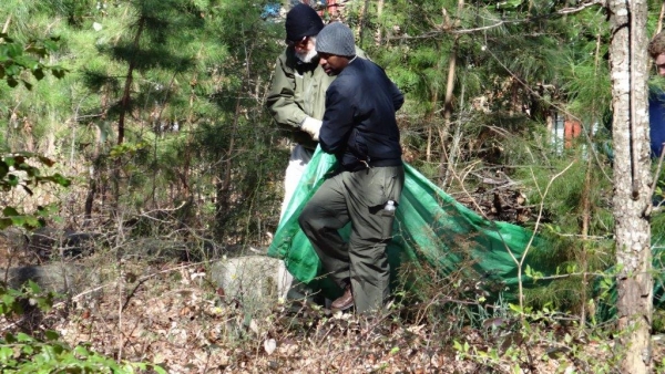 Two volunteers carrying a large green debris bag while cleaning Oberlin Cemetery.